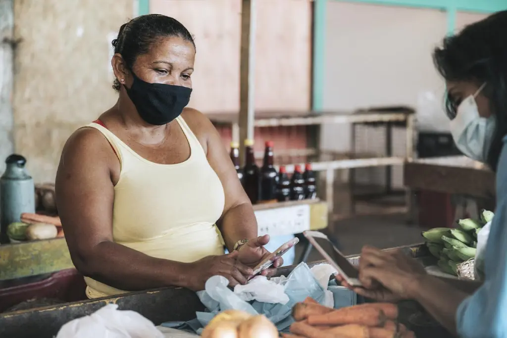 mulher com máscara recebe pagamentos na feira por meio do smartphone