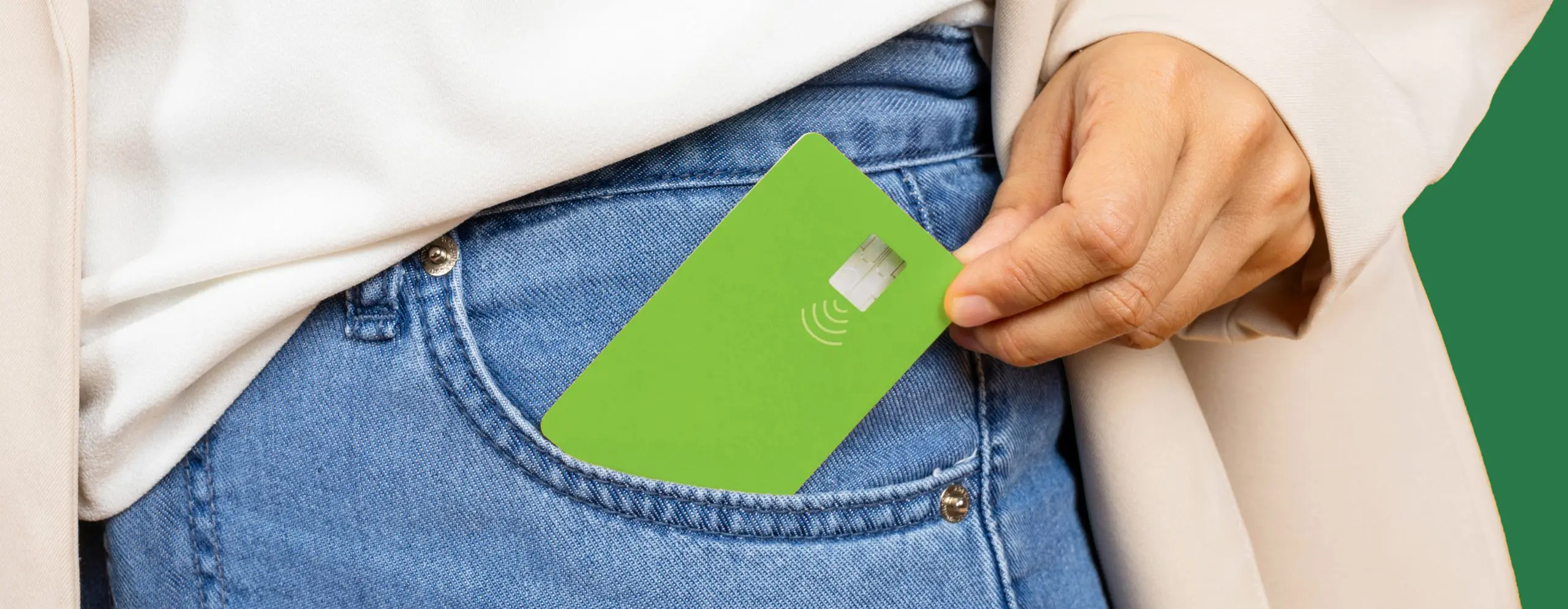 Mulher tirando um cartão de crédito verde do bolso de sua calça jeans.