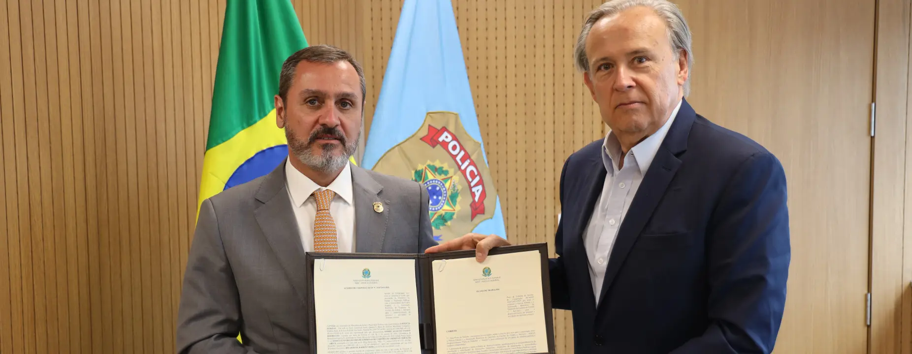 ]Vice-presidente da Abecs e diretor-geral da Polícia Federal seguram documentos de acordo de cooperação técnica, com bandeira do Brasil e brasão da PF ao fundo.